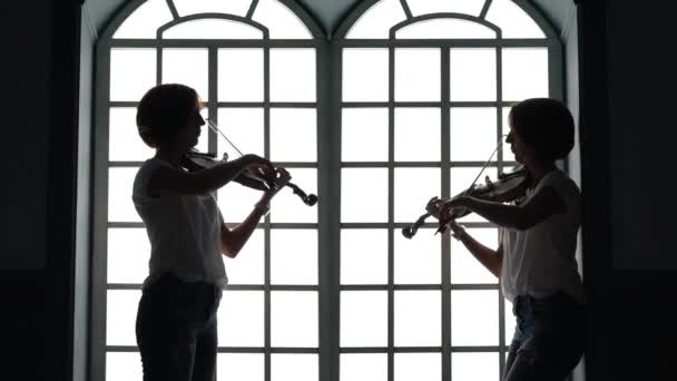 ミュージシャンは、夕方にはウィンドウの背景にバイオリンを果たしています。シルエット — ストック動画