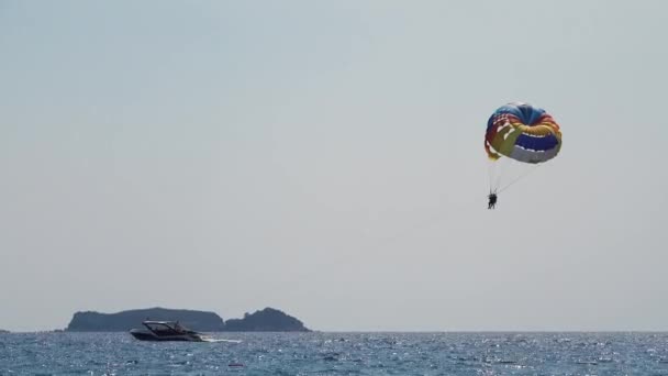 Parasailing achter een boot paar over de zee op een parachute vliegt gebonden met een touw naar de boot — Stockvideo