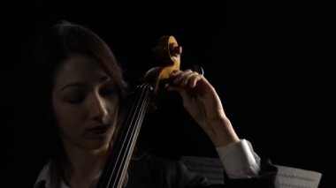 Karanlık bir odada kız çello yapılıyor. Siyah arka plan. Yakın çekim