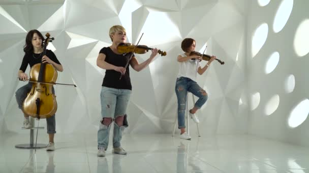 Trio flickor spelar violinerna ett på cello i vita studio — Stockvideo