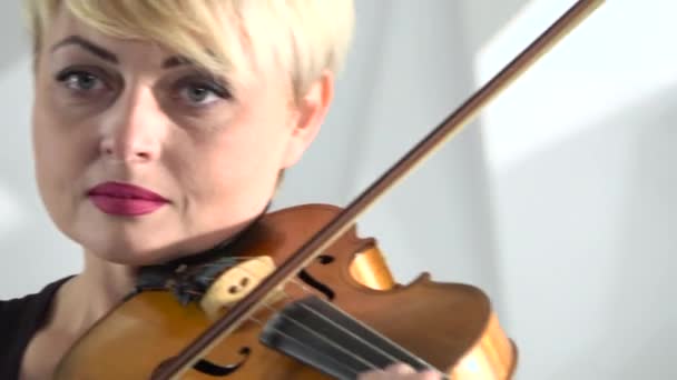 Una donna tiene un violino che la suona inchinandosi sulle corde. Chiudete. Fondo bianco — Video Stock