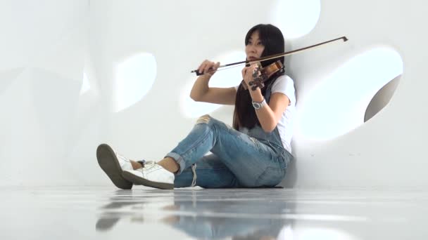 Chica de aspecto asiático sentado en el suelo tocando un violín — Vídeos de Stock