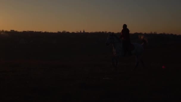 Kobieta siedzi na koniu, którego zawodnik jedzie na koniu na zachód słońca. Zwolnionym tempie. Sylwetka — Wideo stockowe