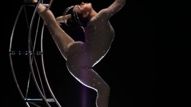 Jimnastikçi bir bir metal yapının ayda dikey bir dize döndürür. Siyah arka plan. Ağır çekim