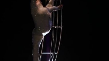 Acrobat bir metal bir yapı içinde dikey bir dize döndürür. Siyah arka plan. Ağır çekim