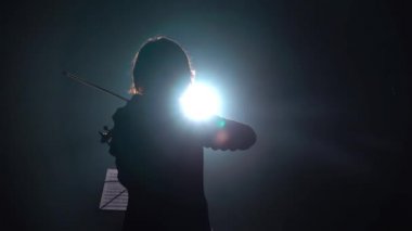 Müzisyen duran sırt ile keman çalıyor. Siyah duman arka plan. Arkadan görünüm