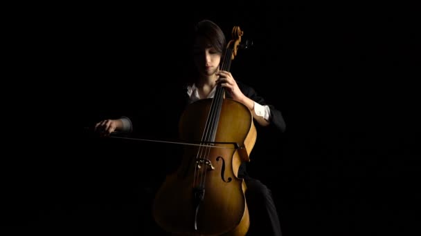 Dívka hraje na violoncello na temné studio. Černé pozadí — Stock video