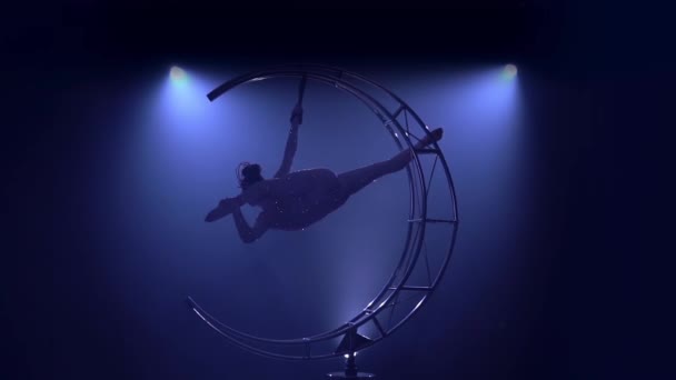 Rhythmic gymnastics in a brilliant costume performs in the air on a metal rotating structure . Blue smoke background. Slow motion — Stock Video