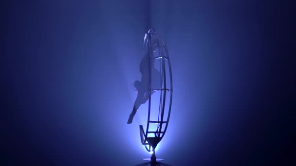 Gymnaste pendu à l'envers dans une ficelle sur une lune de structure tournante. Fond de fumée bleue. Mouvement lent.Silhouette 