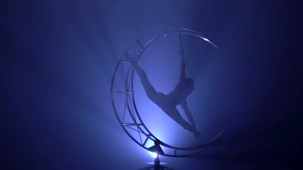 Fille un pèse d'une main dans une ficelle sur une lune comme la construction et elle tourne. Fond de fumée bleue. Mouvement lent.Silhouette 