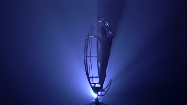 Flicka utför olika krokar i ett mörkt rum på en enhet i form av en snurrande måne. Blå rök bakgrund. Slow motion. Siluett — Stockvideo
