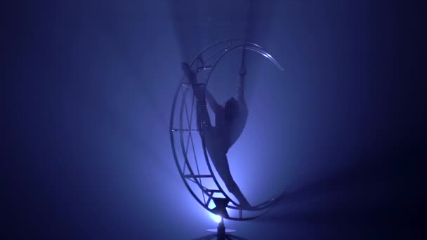 Грациозная гимнастка выполняет трюки над специальным дизайном в темной комнате. Синий дым. Медленное движение. — стоковое видео
