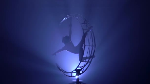 Gymnaste un design rotatif dans un studio sombre. Fond de fumée bleue. Mouvement lent.Silhouette 