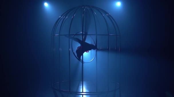 Chica en una jaula acrobacias en un aro en un cuarto oscuro. Fondo de humo azul. Silueta. Movimiento lento — Vídeo de stock