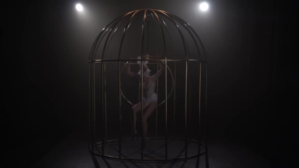 Toespraak op podium meisje in een kooi spinnen op de lucht hoepel. Zwarte rook achtergrond. Slow motion — Stockvideo