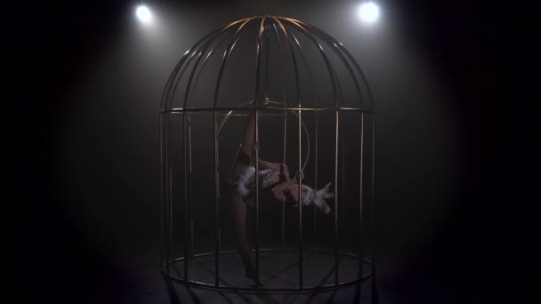 Turnerin auf der Bühne in einem Käfig, der sich am Luftkorb dreht. schwarzer Rauchhintergrund. Zeitlupe — Stockvideo