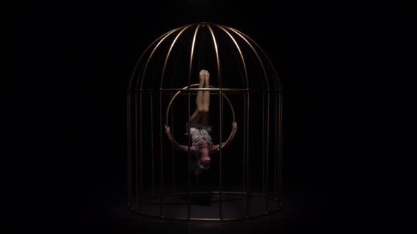 Antenne acrobatiek op een roterende hoepel in een kooi kamer. Zwarte achtergrond. Slow motion — Stockvideo
