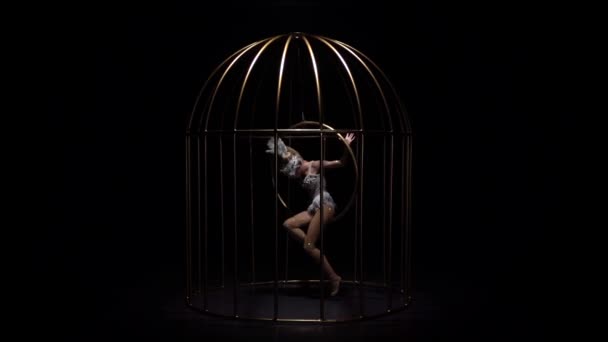 Gimnastyczka w kostium ptaka jazda hoop w klatce na ciemnej scenie. Czarne tło. Zwolnionym tempie — Wideo stockowe