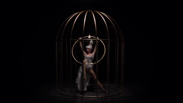 Chica girando en un aro en una jaula de oro. Fondo negro. Movimiento lento — Vídeos de Stock