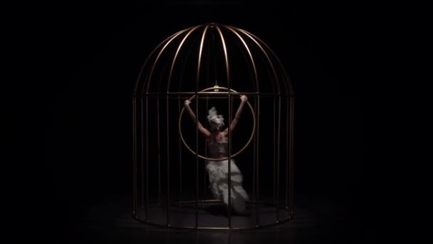 女体操运动员在黑暗的舞台上的笼子里骑着吊环。黑色背景。慢动作 — 图库视频影像