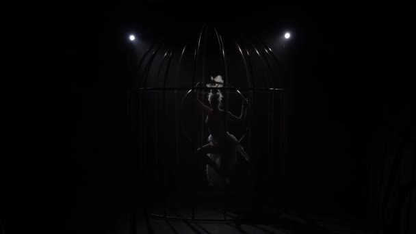 Girl on a rotating hoop in a cage in a dark room. Black background. Silhouette. Slow motion — Stock Video