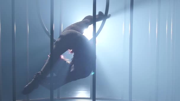 Acrobat in a gymnastic hoop it is spinning a on a smoke scene in a cage. Smoke background. Slow motion. Close up. Silhouette — Stock Video