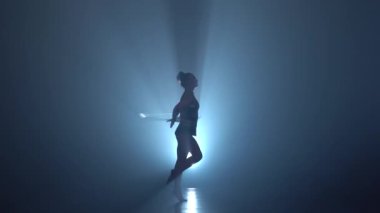 Kız jimnastikçi ellerinin üzerinde hileler çemberler ile gerçekleştirir ve bacağını havaya kaldırdı. Duman arka plan. Siluet