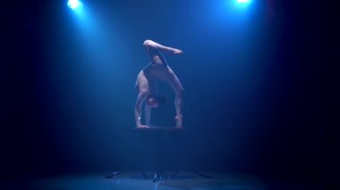 Kız jimnastikçi çeşitli akrobasi bir tablo üzerinde gerçekleştirir. Mavi renkli duman. Ağır çekim