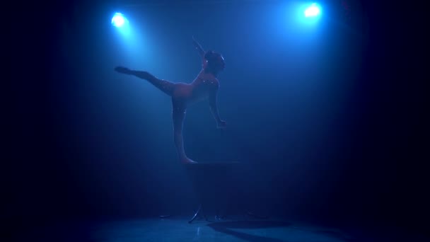 Гімнастка виконує трюки на столі в студії. Синій дим фону. Силует — стокове відео