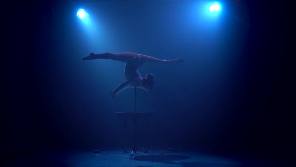 Acrobat meisje op het podium doet acrobatische stunts permanent op haar handen. Roken blauwe achtergrond. Silhouet — Stockvideo