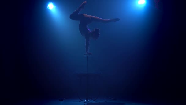 La chica en el escenario hace acrobacias de pie sobre sus manos. Fondo azul humo. Silueta — Vídeos de Stock