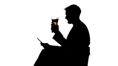 Adam bir bardak bira içiyor ve smartphone kaydırır. Yan görünümü. Beyaz arka plan siluet