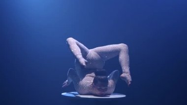 Acrobat kız baş aşağı duran bir tablo üzerinde döner. Mavi renkli duman. Ağır çekim