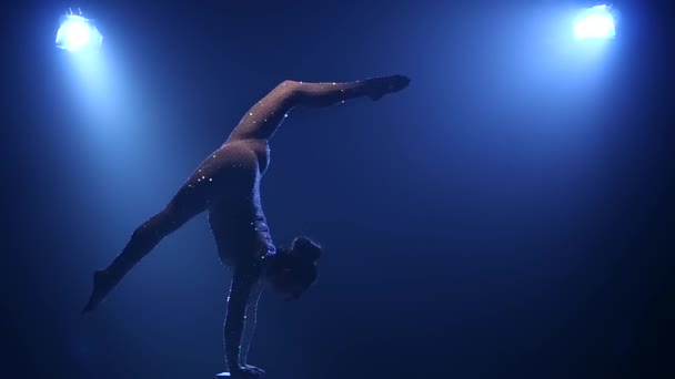 Gymnastka provádí akrobacie na stole v temné studio. Kouř modré pozadí. Zpomalený pohyb. Silueta — Stock video