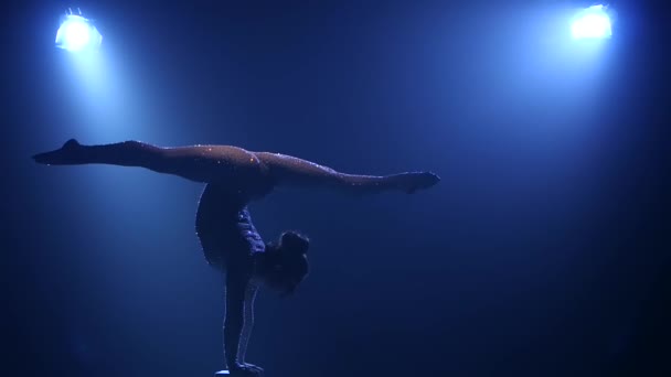 Gimnasta hace varios movimientos mientras está de pie en él. Fondo azul humo. En cámara lenta. Silueta — Vídeo de stock