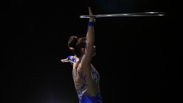 Дівчина-гімнастка повертає металевий кільце на руку, а потім на ногу. Чорний фон. Повільний рух — стокове відео