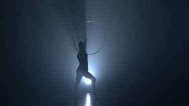 Jimnastikçi kasnak kollarında döner ve bacağını yukarı yükseltir. Ağır çekim. Duman arka plan. Siluet