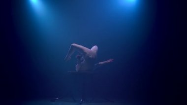 Acrobat kız baş aşağı duran bir tablo üzerinde döner. Mavi renkli duman. Ağır çekim