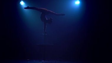 Jimnastikçi masanın üzerinde akrobatik stunts gösterir. Mavi renkli duman. Ağır çekim. Siluet