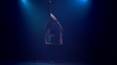 Jimnastikçi masanın üzerinde akrobatik stunts gösterir. Mavi renkli duman. Ağır çekim