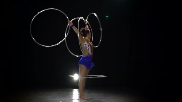 Girl gymnast twists a lot of metal hoops on her body. Black background. Slow motion — Stock Video