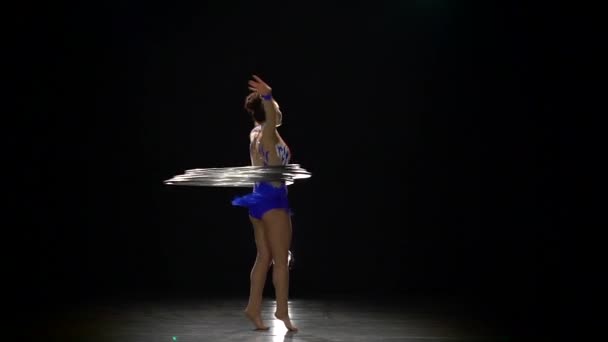 Κορίτσι gymnast περιστρέφεται γύρω από με πολλά μεταλλικά τσέρκια. Αργή κίνηση. Μαύρο φόντο — Αρχείο Βίντεο