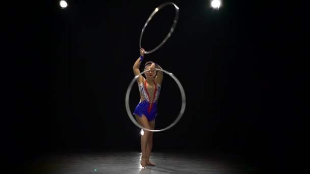 Gymnast twists the hoops in the air and dances . Slow motion. Black background — Stock Video