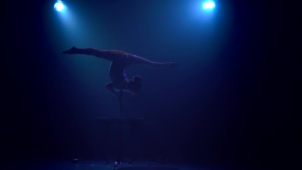 Гімнастка в повітрі стоячи догори дном робить трюк на столі. Синій дим фону. Повільний рух. Силует — стокове відео