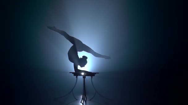 Gymnast performs tricks on the table in the studio . Smoke background. Slow motion. Silhouette — Stock Video