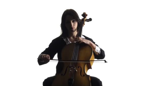 La chica en una habitación se sienta y toca un violonchelo. Fondo blanco — Vídeo de stock