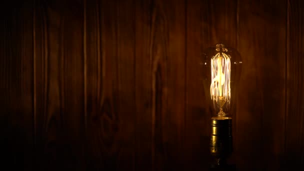 Alte Vintage Edison Glühbirne glüht auf dem Hintergrund von Holzplanken — Stockvideo