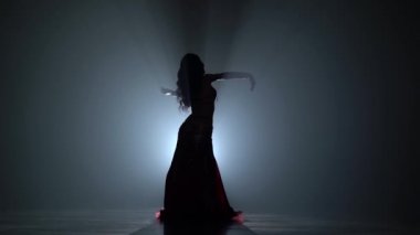 Kadın bir oryantal dans karanlık stüdyoda gerçekleştiriliyor. Duman arka plan. Sihouette