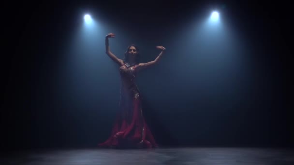 Menina começa a dançar dança do ventre no estúdio escuro. Fundo de fumo preto. Movimento lento — Vídeo de Stock