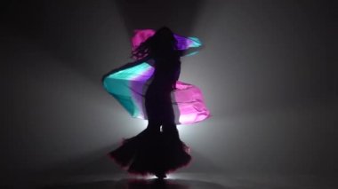 Kadın çok renkli şal ile oryantal dans dans başlar. Sihouette, hayır. Siyah duman arka plan. Yavaş hareket